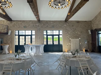 Salle lumineuse en pierre – location mariage à Béziers Salle de mariage en pierre à Béziers avec poutres apparentes et tables dressées, lumineuse.